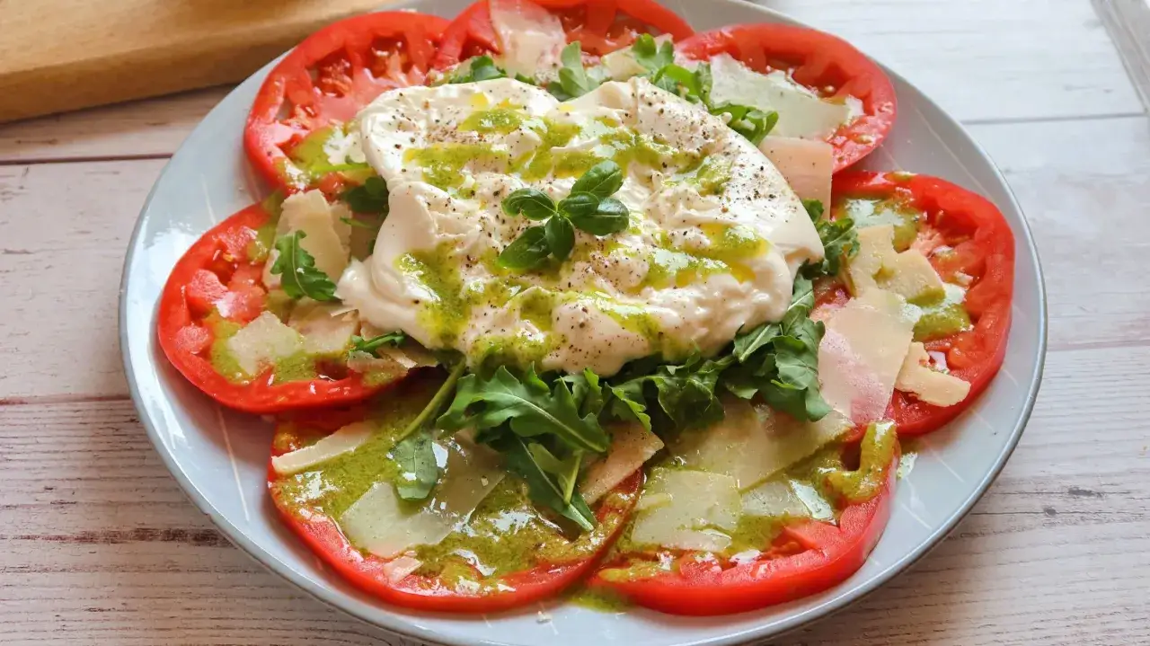 Deliciosa ensalada de burrata con rodajas de tomate, rúcula, queso parmesano y aderezo verde.
