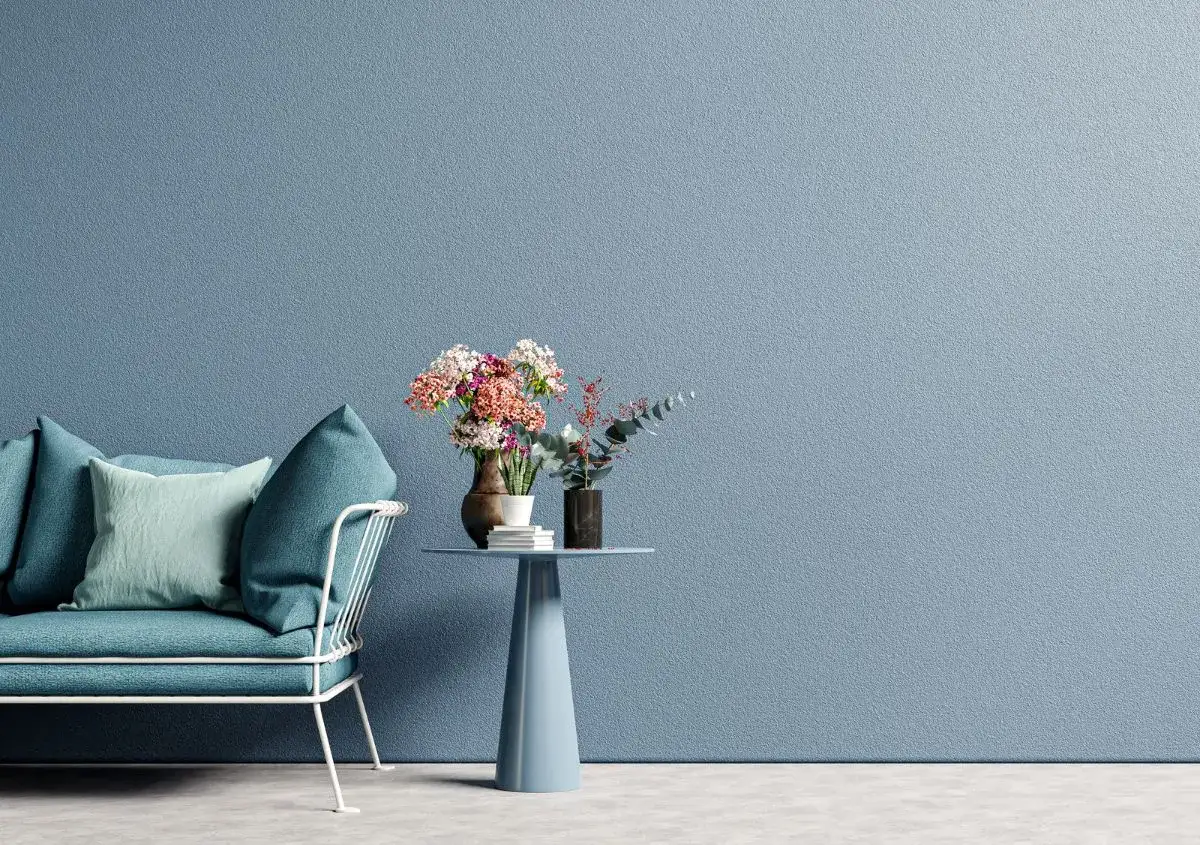 Divano blu petrolio e tavolino con fiori su pareti azzurre. I colori pareti creano un'atmosfera rilassante.