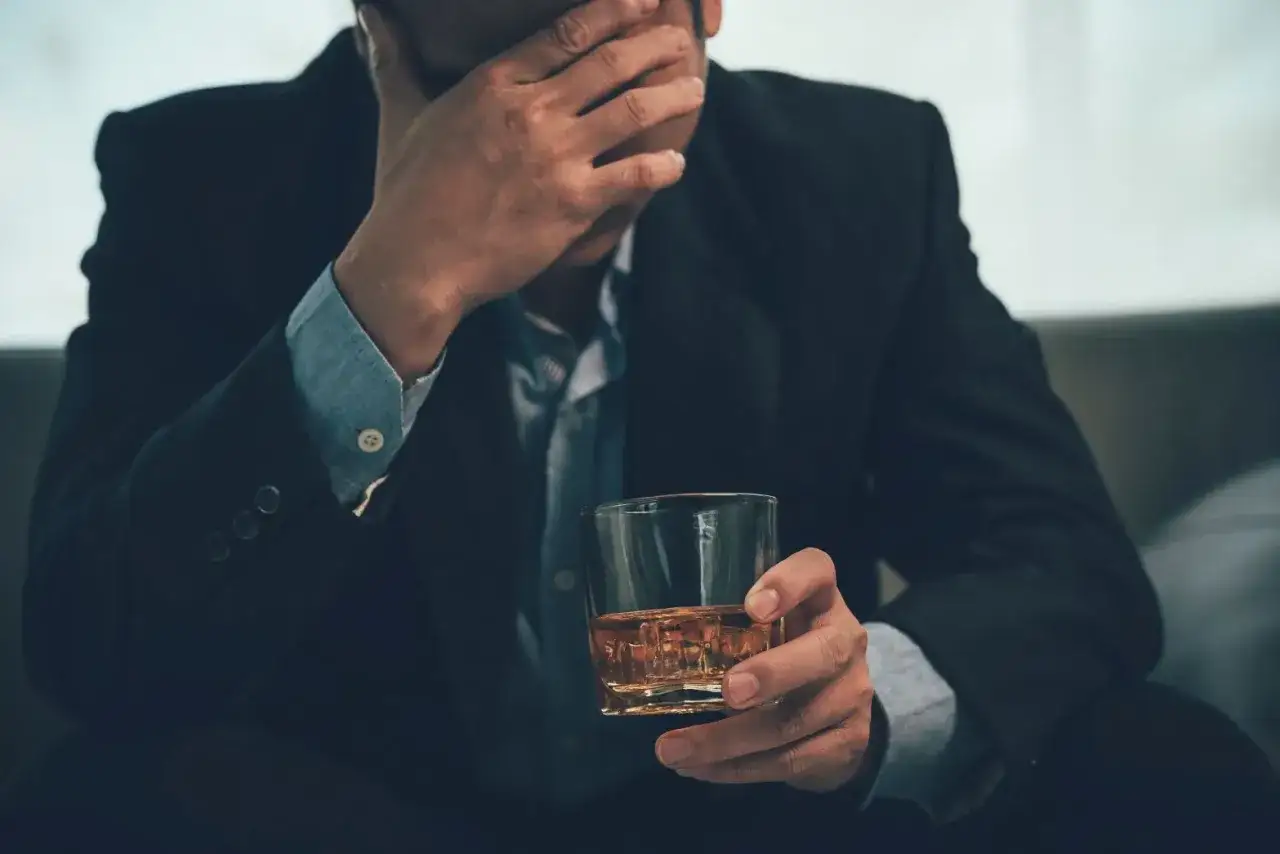 Zmartwiony mężczyzna w garniturze trzyma szklankę z whisky. Zastanawia się, renta alkoholowa ile wynosi.