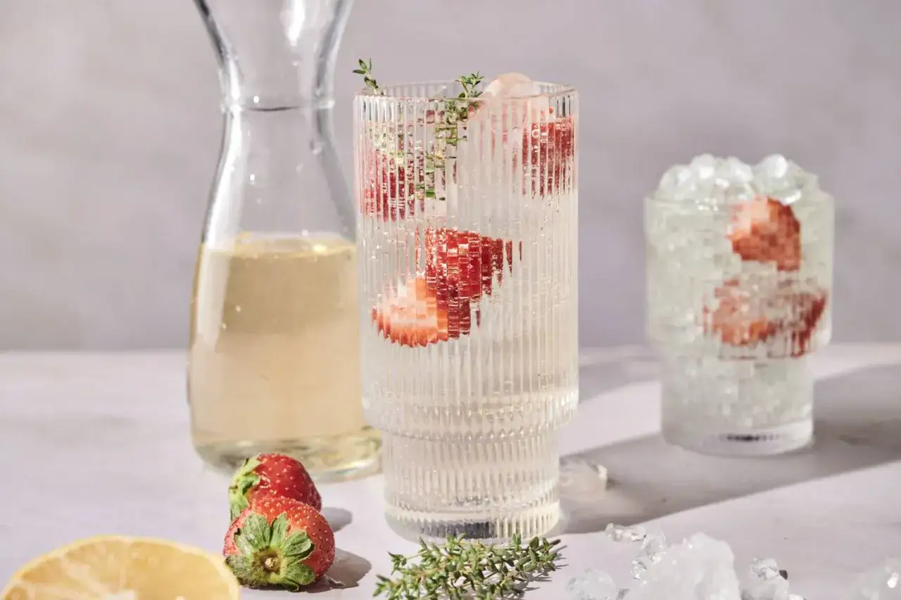 Orzeźwiający drink z truskawkami i lodem, obok karafka z winem półwytrawnym i cytryna.