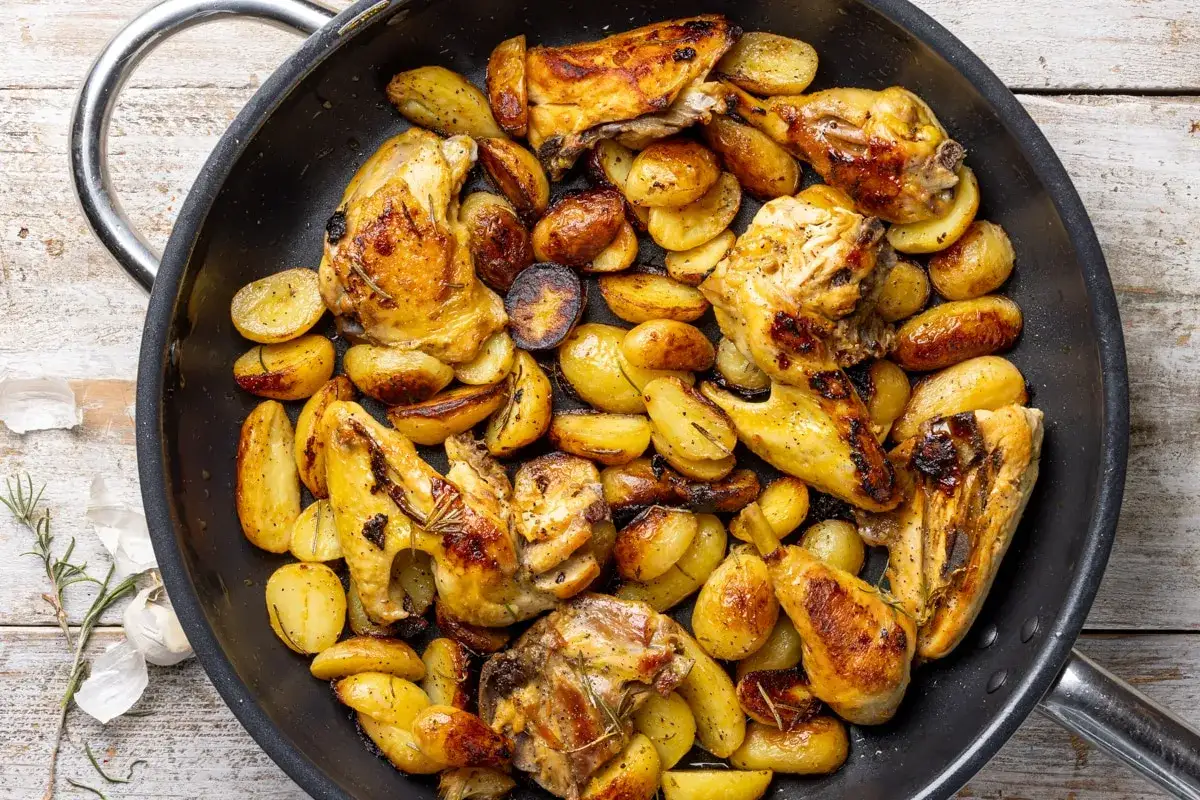 Pollo con patate in padella, dorato e saporito, con erbe aromatiche. Un piatto invitante pronto per essere gustato.