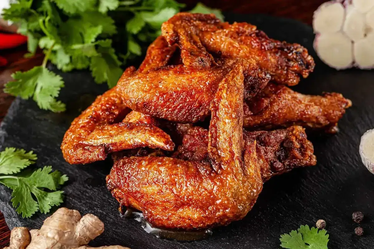 Aromatiche alette di pollo dorate e succulente, servite su una pietra scura con zenzero, aglio e coriandolo fresco.