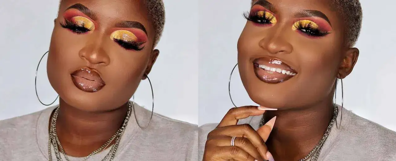 En kvinna med dramatisk makeup, inklusive f&auml;rgstark &ouml;gonskugga och markerade &ouml;gonfransar, framh&auml;ver sina hooded eyes. Hon b&auml;r stora silver&ouml;rh&auml;ngen och flera halsband.