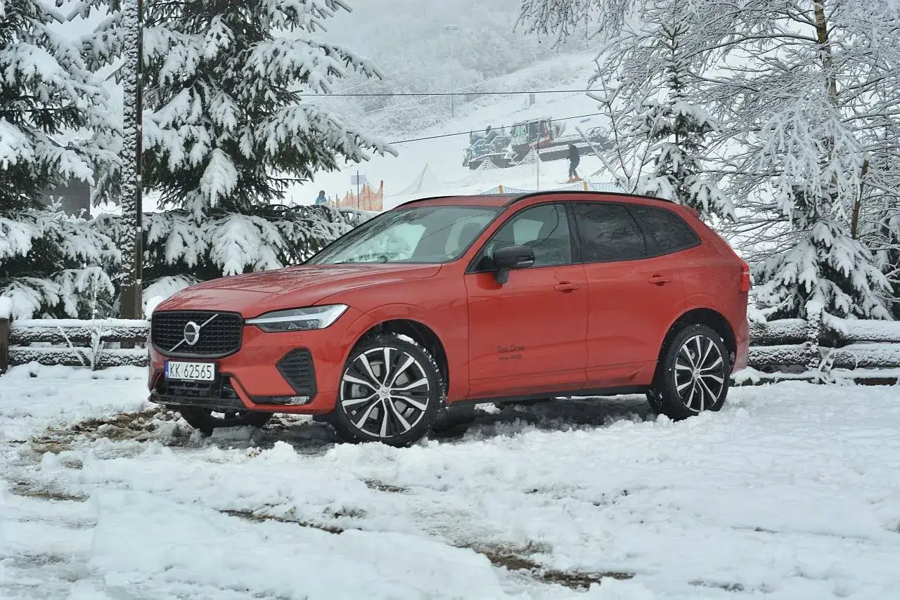 Pomarańczowe Volvo XC60 T6 na tle zaśnieżonych drzew i stoku narciarskiego.