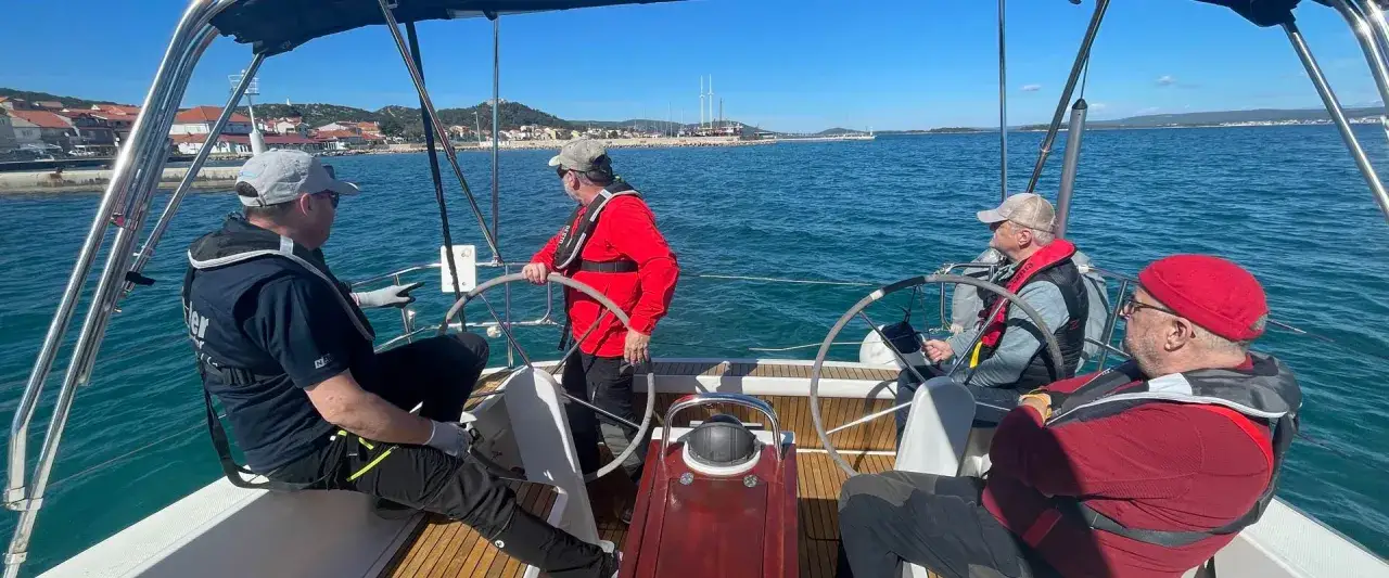 Uomini in barca a vela durante un corso skipper, con un istruttore che spiega le manovre.