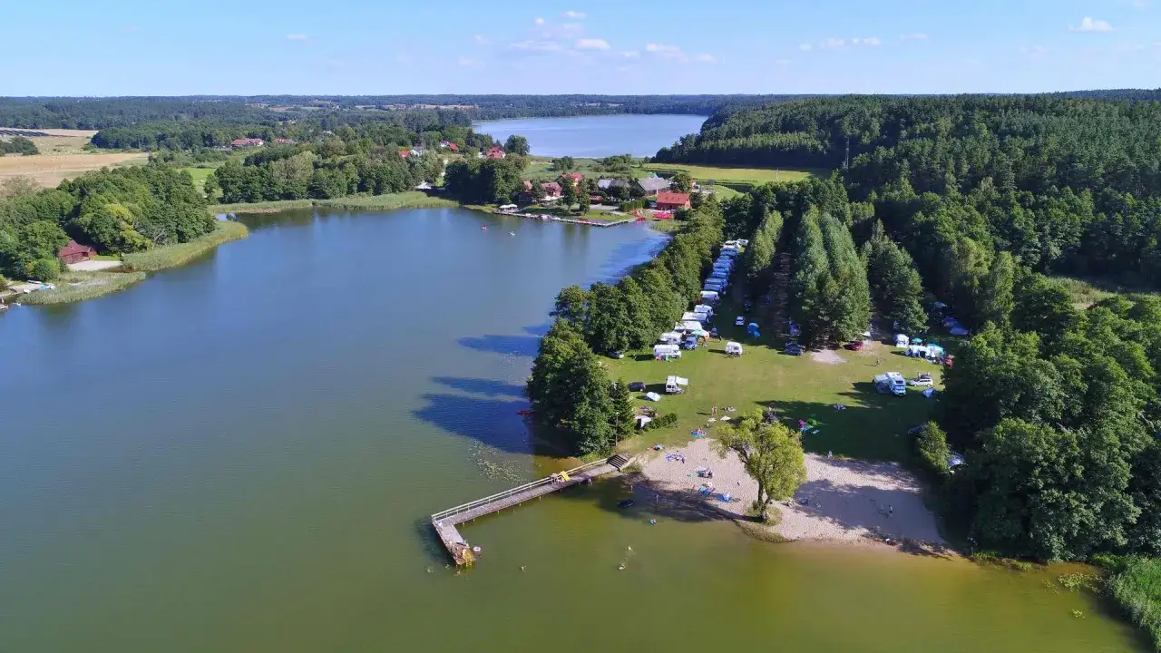 Pola namiotowe Mazury nad jeziorem, z kamperami, namiotami i plażą.