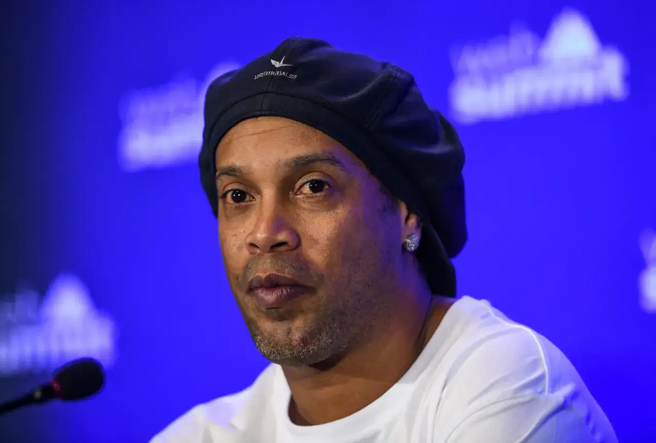 Ronaldinho w czapce i białej koszulce, z kolczykiem w uchu. W tle niebieskie tło. Ile Ronaldinho ma lat?