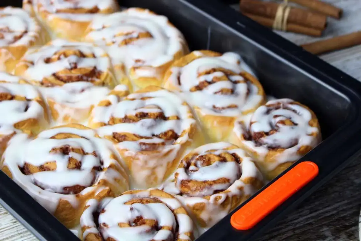 Deliciosos rollitos de canela recién horneados, cubiertos con un glaseado blanco cremoso, listos para ser disfrutados.