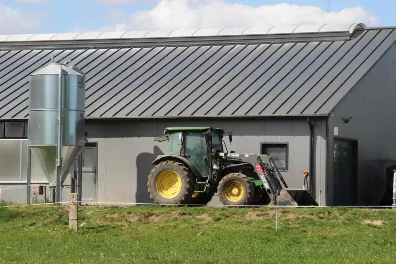Zielony traktor z ładowaczem przed nowoczesnym budynkiem gospodarczym. Aktywny rolnik korzysta z dopłat do inwestycji.