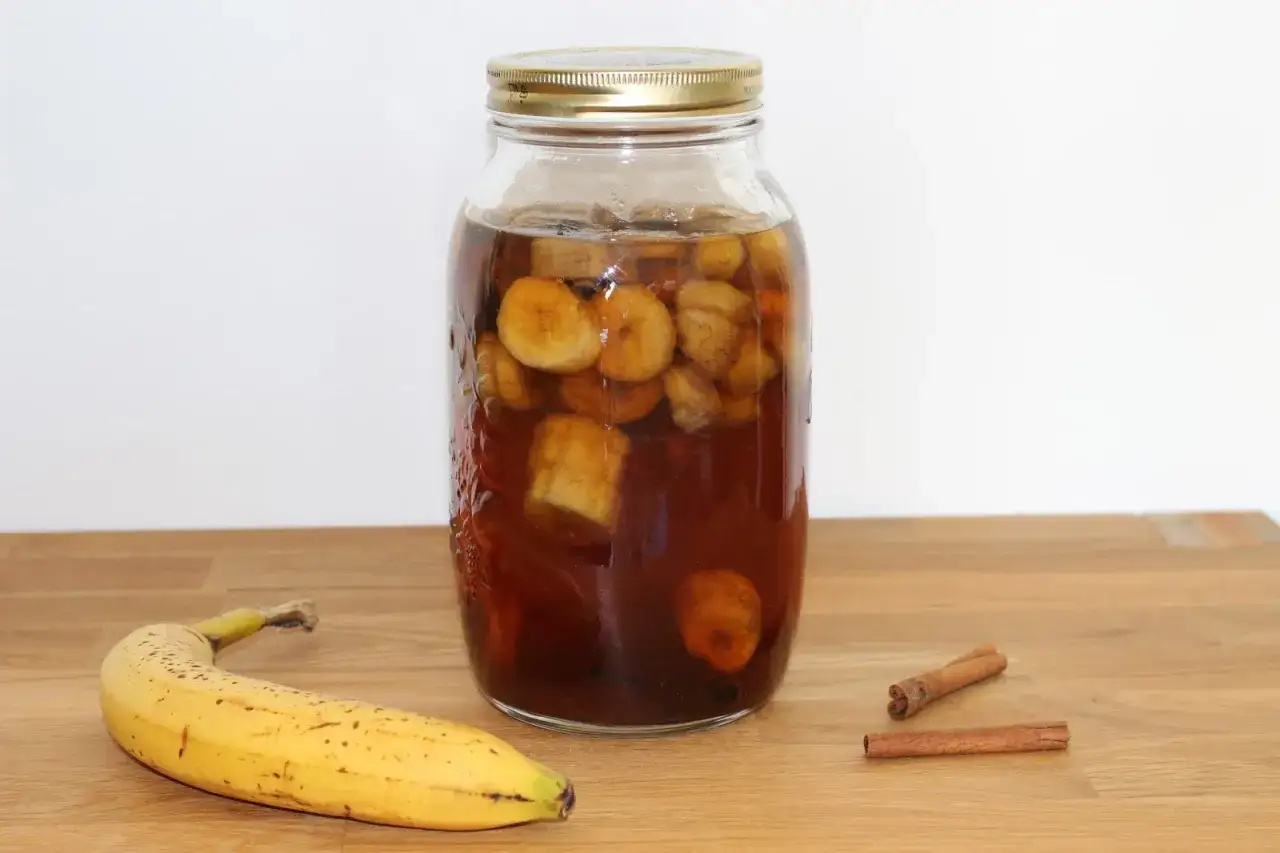 Bocal de rhum arrangé banane, avec des rondelles de banane, des bâtons de cannelle et un rhum ambré. Une recette maison pour un délice tropical.