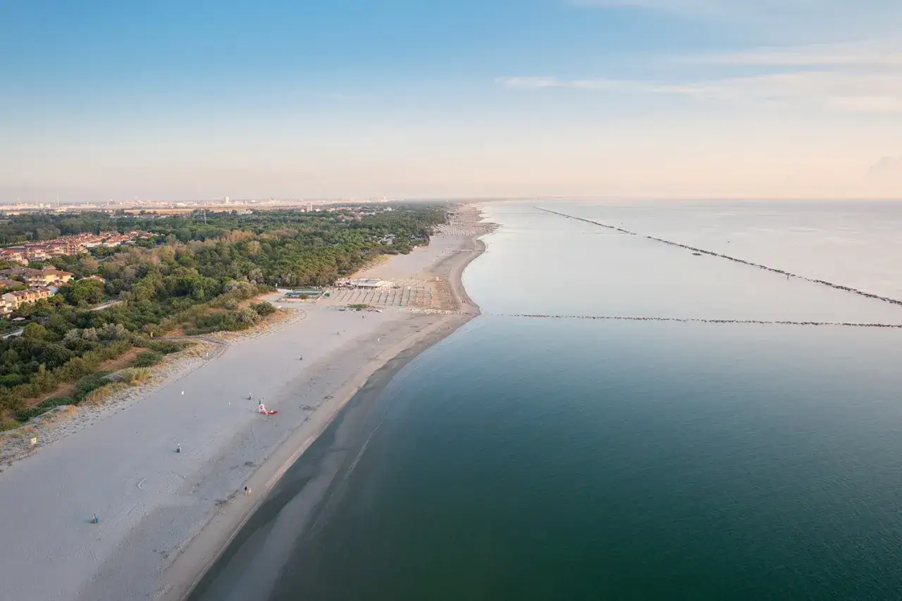 Lunga spiaggia dorata con ombrelloni ordinati, vegetazione lussureggiante e il mare calmo. Un vero mare lido di classe.