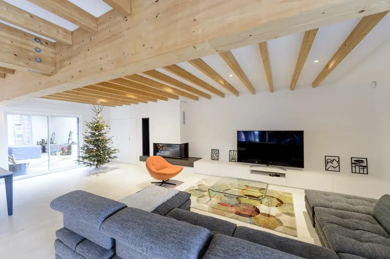 Salon moderne avec une **poutre apparente** en bois, un sapin de Noël, un canapé gris et une cheminée.