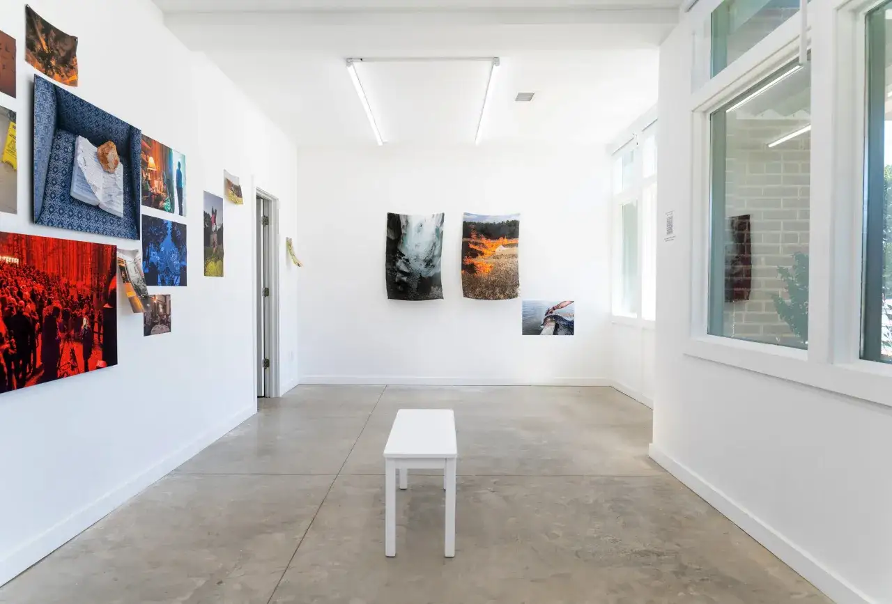 Art exhibition at the Atlanta Center for Photography, featuring diverse photographic works on white walls, with a minimalist bench in the center.