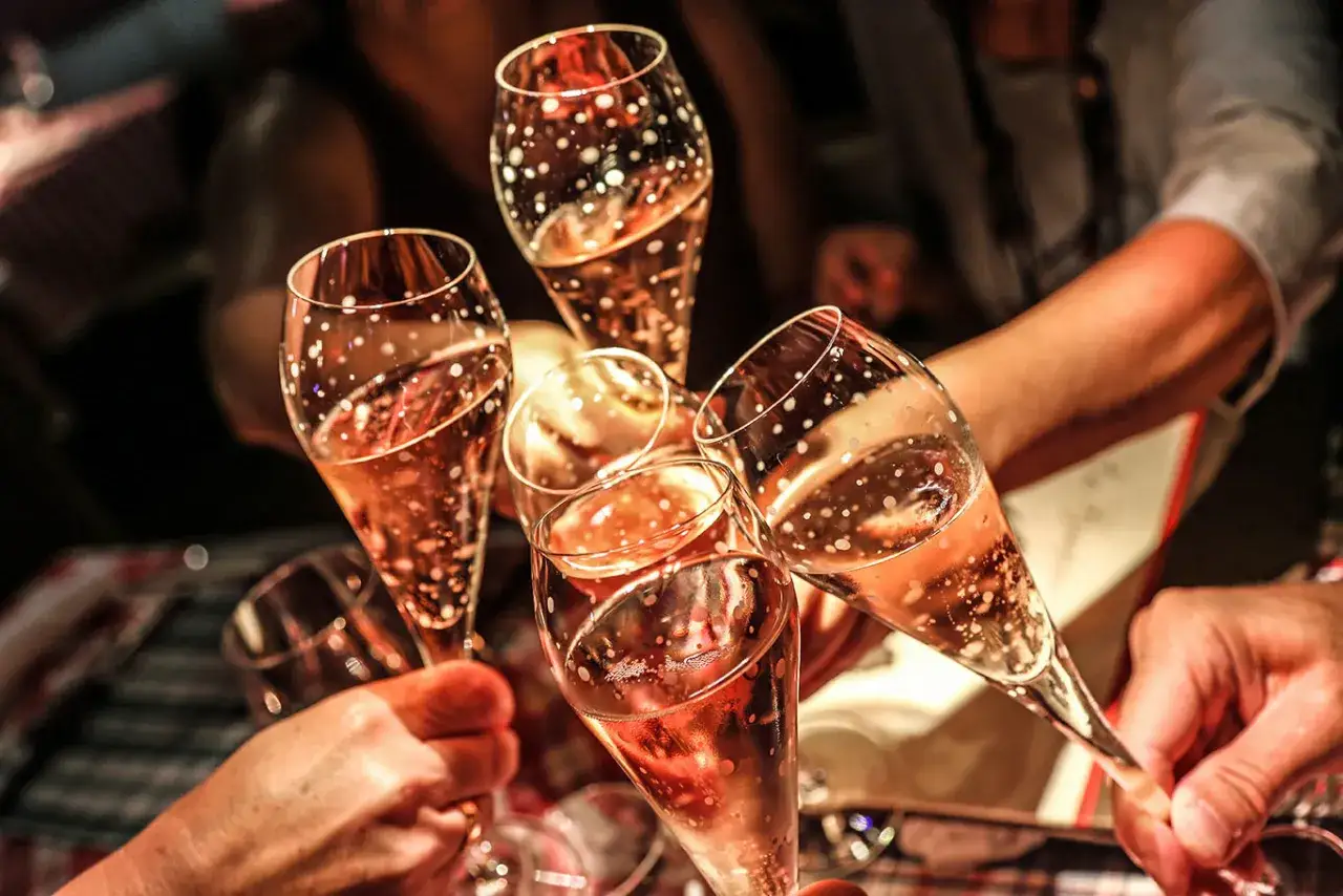Hände halten Gläser mit sprudelndem Roséwein, um einen Toast auszusprechen.