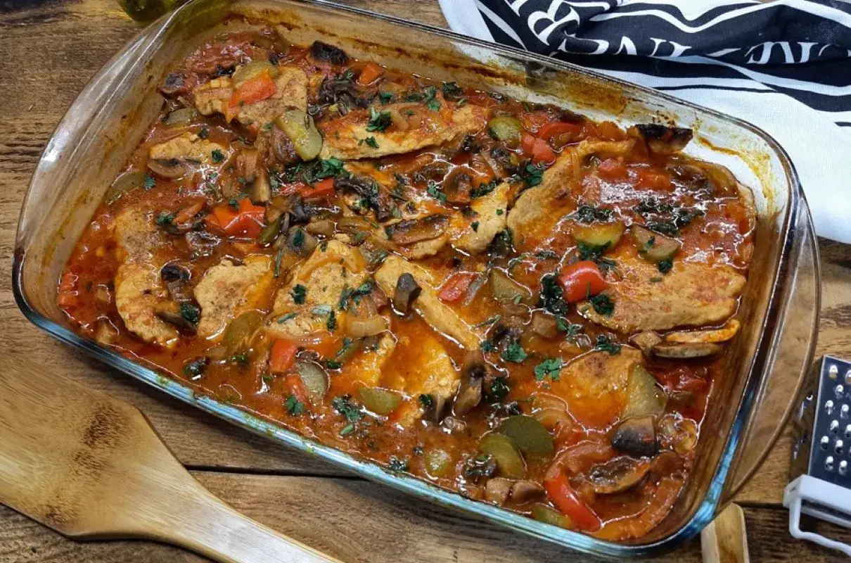 Soczysty schab po cygańsku w sosie pomidorowym z pieczarkami i papryką, posypany natką pietruszki. Pyszne danie w naczyniu żaroodpornym.