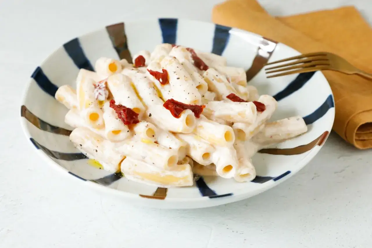Piatto di pasta cremosa con pesto, pomodori secchi e ricotta, guarnito con pepe nero.