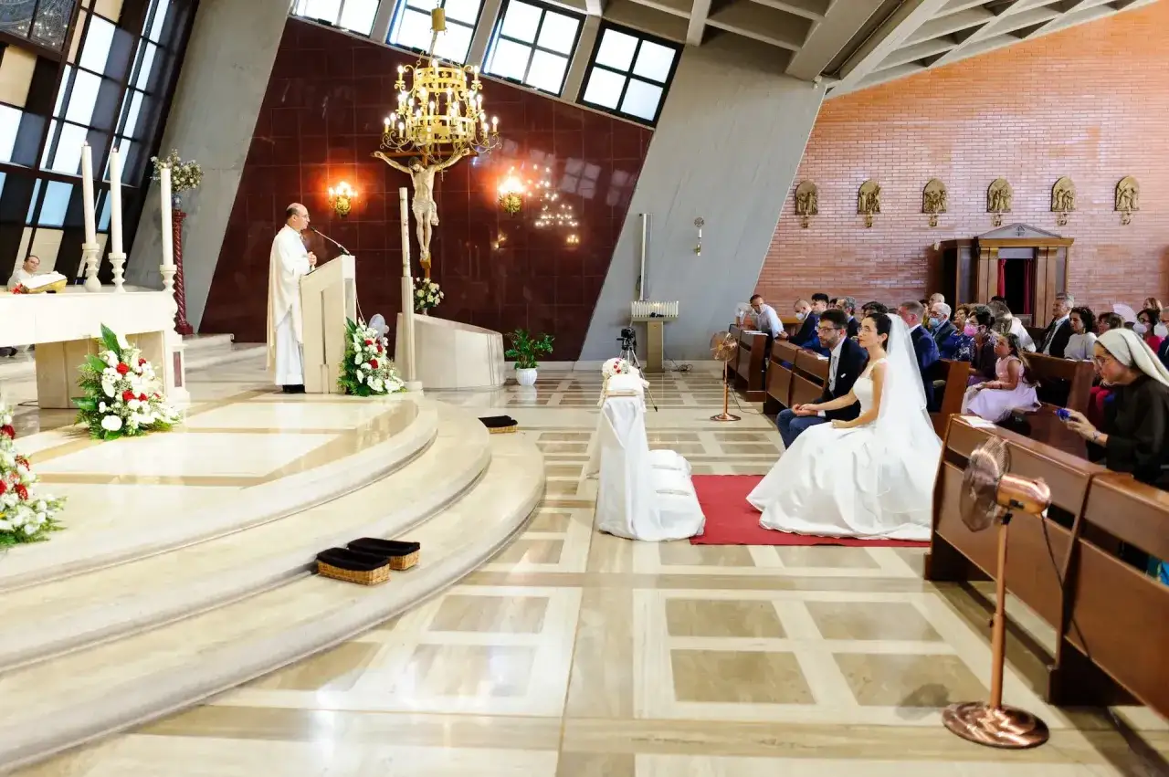 Brudens sida i kyrkan. Brudparet sitter på första bänkraden, omgivna av gäster. Prästen står vid altaret.