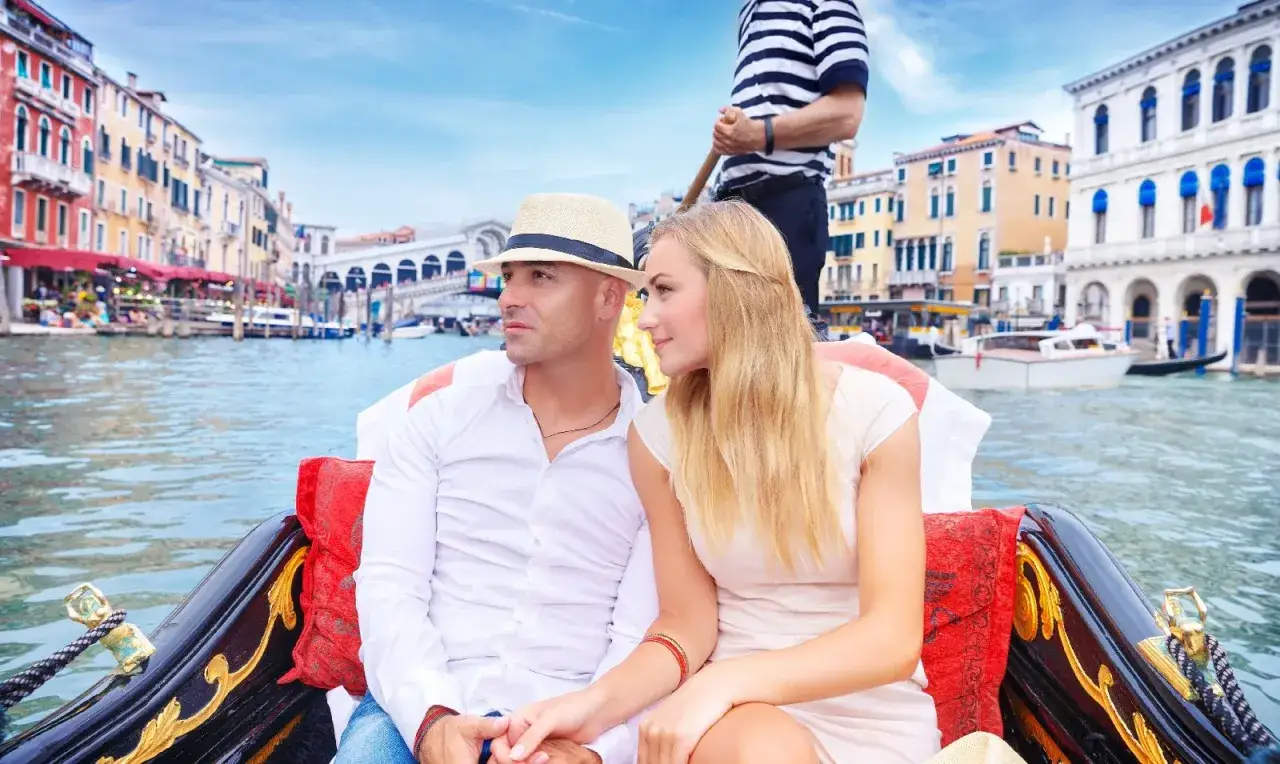 Coppia su gondola a Venezia, con gondoliere sullo sfondo. Chissà quanto guadagna un gondoliere per un giro così romantico.