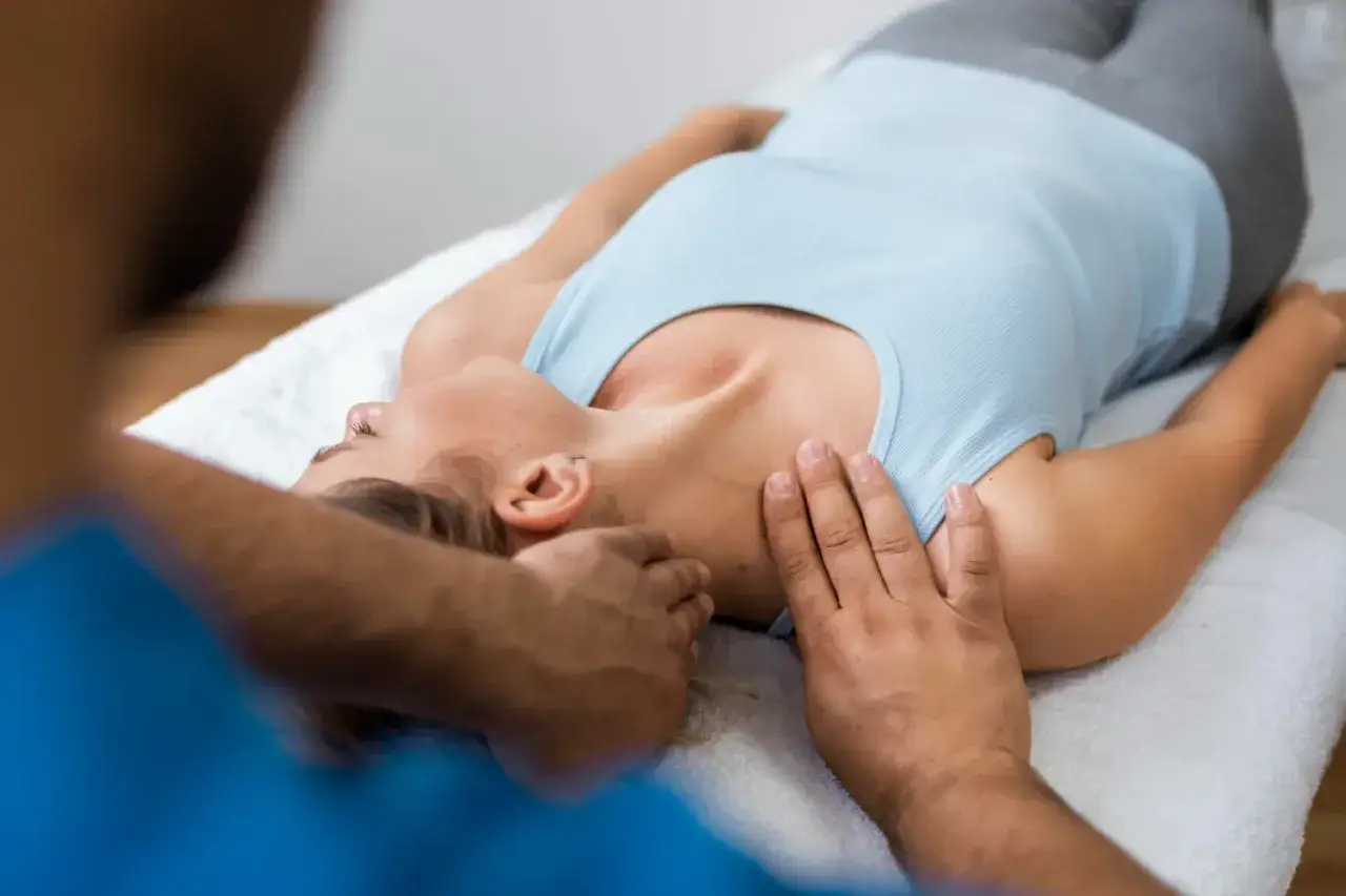 Terapeuta delikatnie uciska szyję pacjentki, łagodząc objawy po nastawieniu kręgosłupa.
