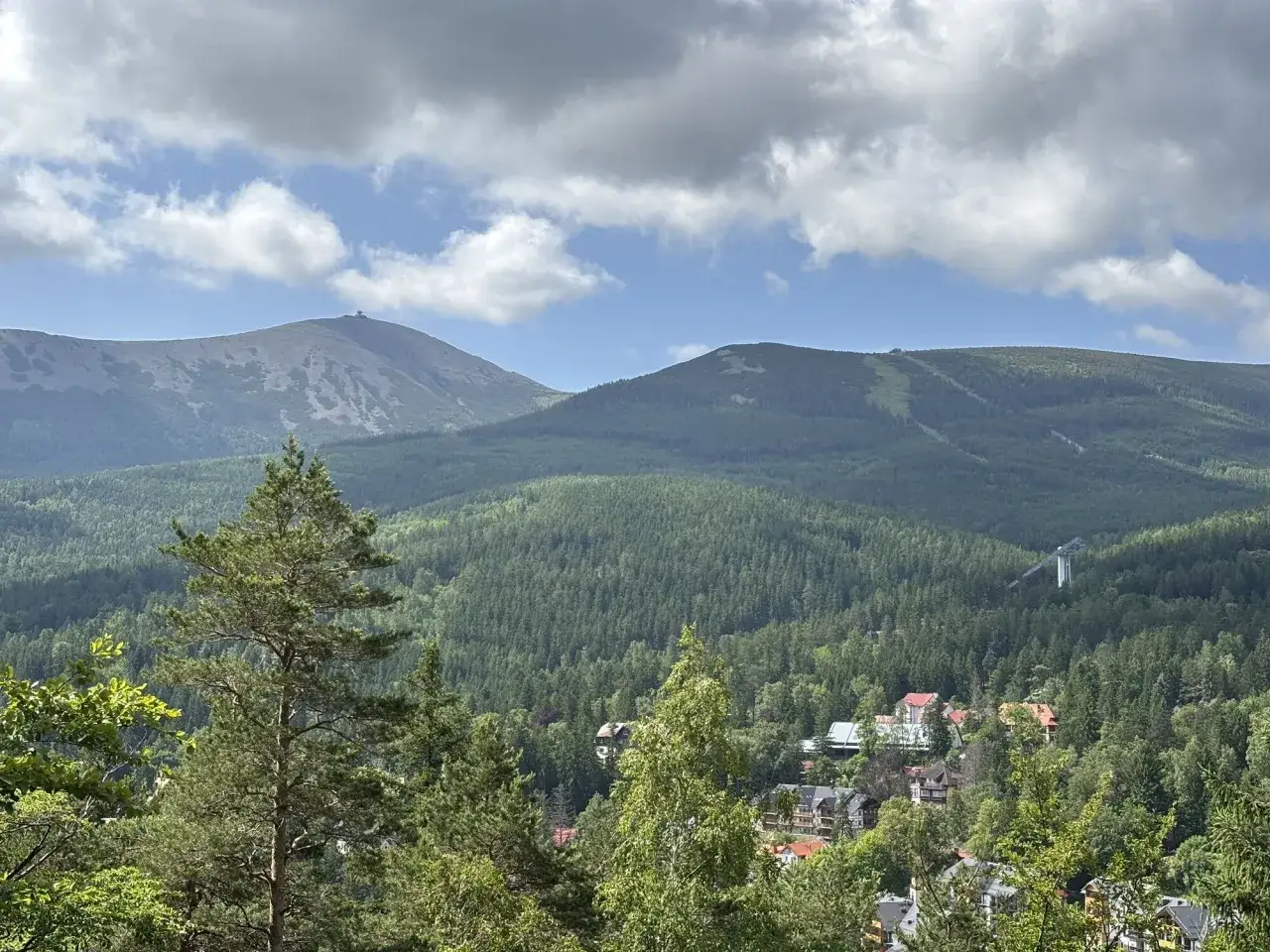 Widok na góry Karkonosze z Karpaczem. W oddali szczyt Śnieżki, a niżej lasy i zabudowania.