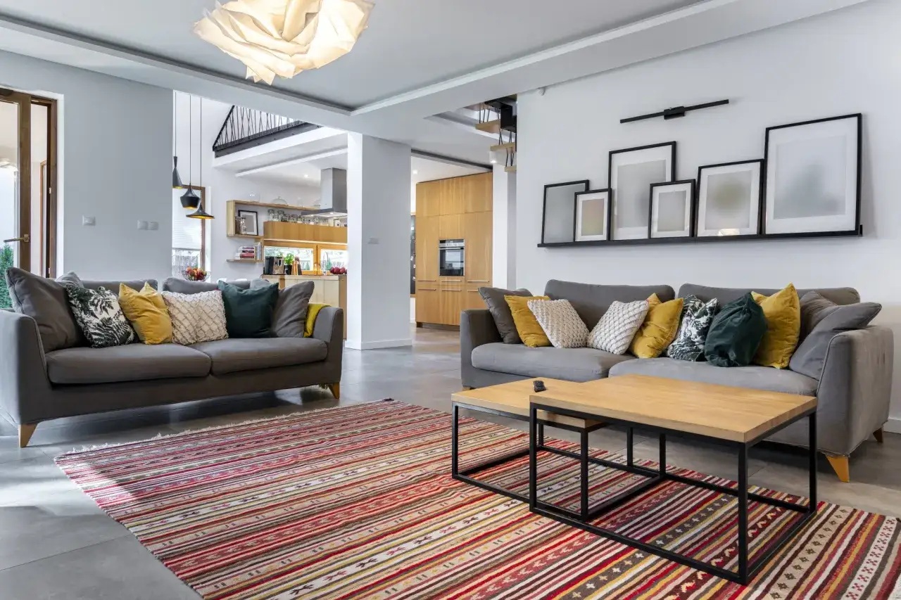 Canapé gris clair avec coussins jaune moutarde et vert forêt. Le tapis rayé rouge et jaune répond à la question : quelle couleur va avec le gris clair.