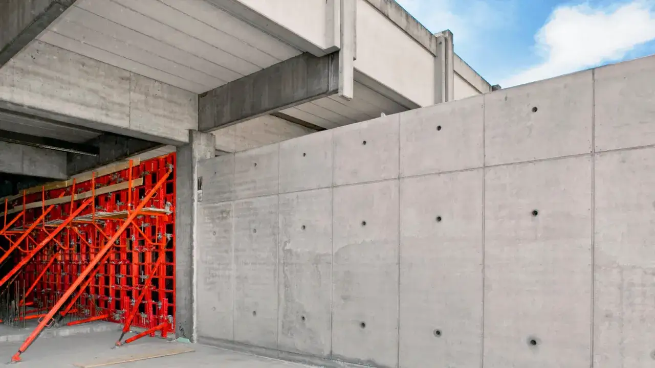 Rote Schalung für Sichtbeton-Wände, die gerade gegossen werden. Betonfertigteile und Bewehrung sind sichtbar.