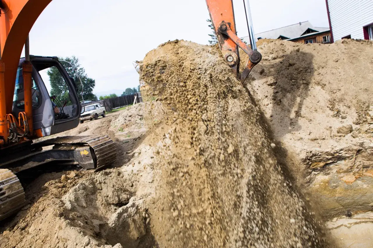 Koparka wykonuje wykop pod fundament, sypiąc ziemię na stos.