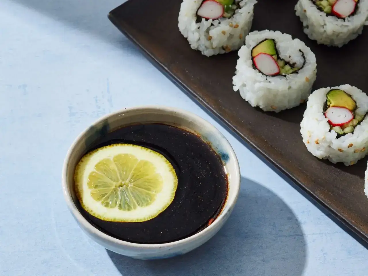 Idealne co do sushi: rolki z awokado i paluszkami krabowymi, zanurzone w sosie sojowym z plasterkiem cytryny.