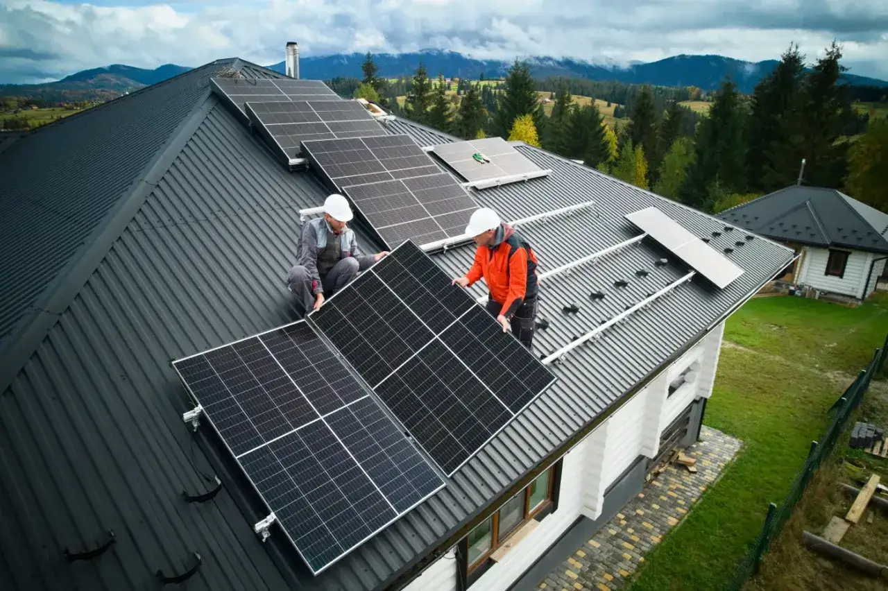 Dwóch mężczyzn montuje panele słoneczne na dachu domu. Stają się prosumentami, czerpiąc energię ze słońca.