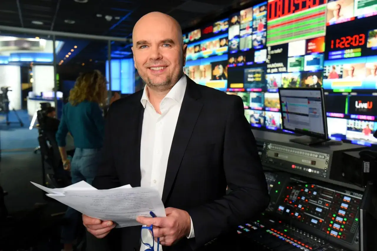 Prezenter w studiu TVN Fakty, wśród ekranów i sprzętu. W rękach trzyma dokumenty.