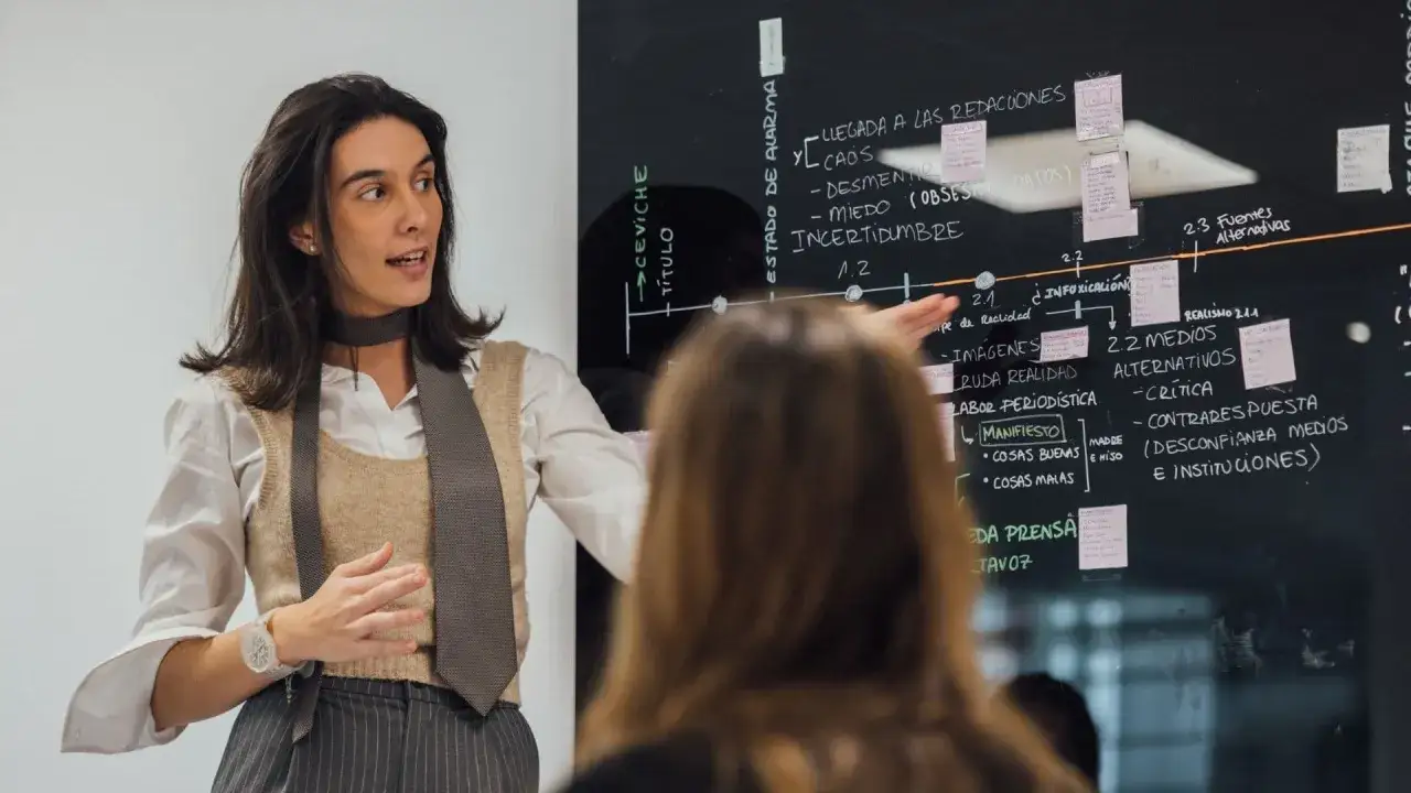 Mujer explica un diagrama en pizarra, detallando 