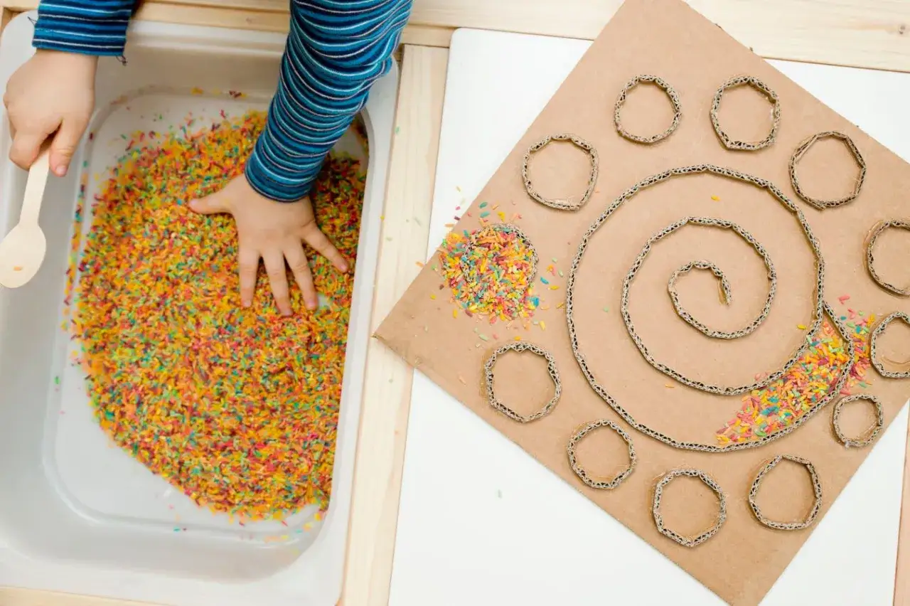 Niño explorando diferentes tipos de texturas para niños con arroz de colores y cartón.