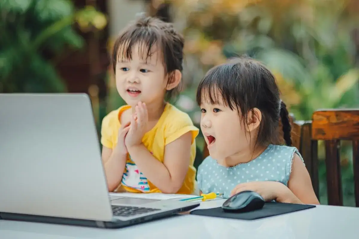 Dwie dziewczynki patrzą na laptopa. Zastanawiasz się, jak zablokować internet w telefonie dziecka?