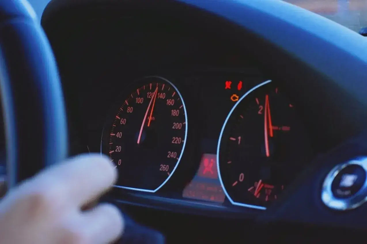 Arm am Lenkrad, Tacho zeigt 120 km/h. Warnleuchten leuchten auf, mögliche Motorschaden Symptome.