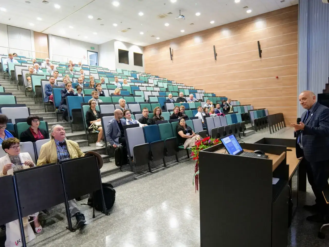 Wykład na studiach prawniczych: aula z siedzącymi słuchaczami i wykładowcą przy m&oacute;wnicy.