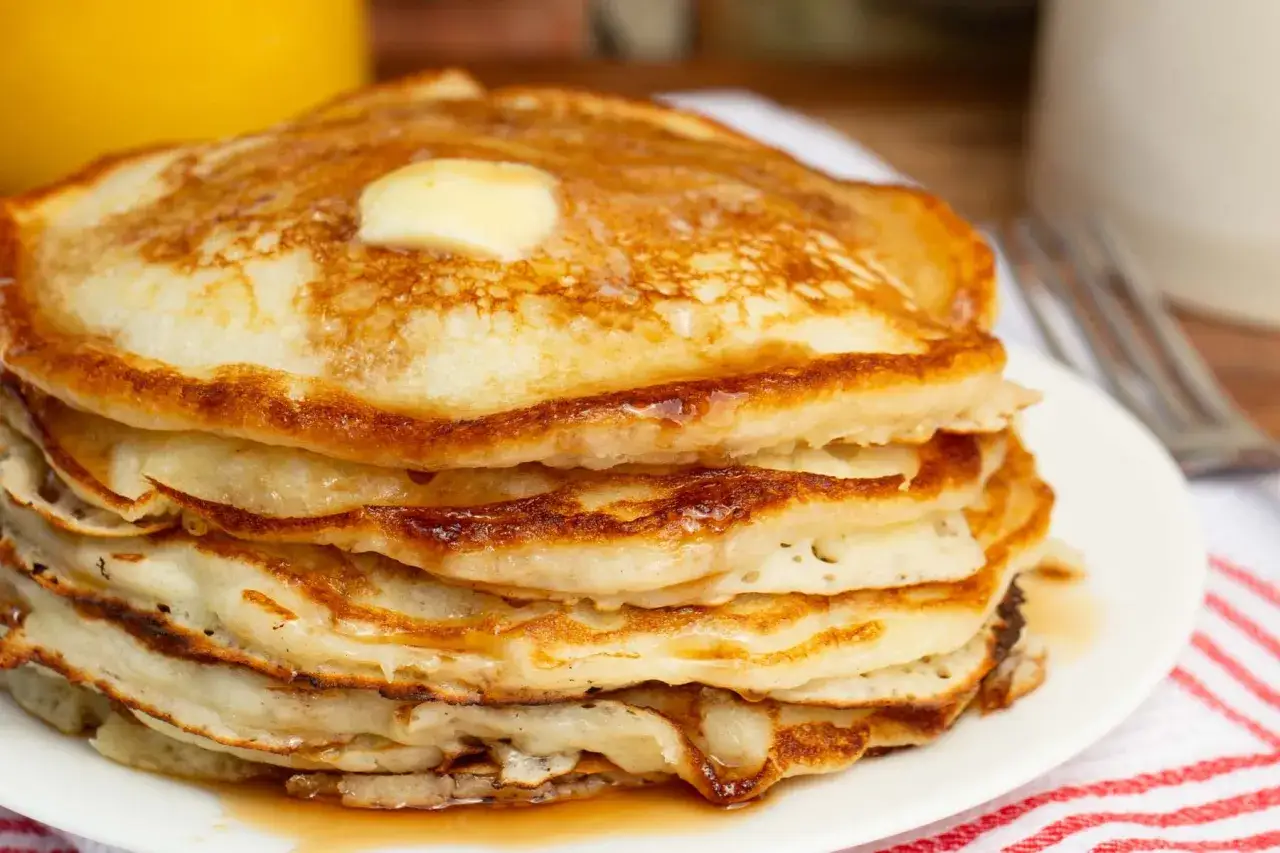 Una pila de tortitas doradas, cubiertas con una generosa porción de mantequilla derretida y sirope. ¡Un desayuno perfecto de tortitas sin mantequilla añadida a la masa!