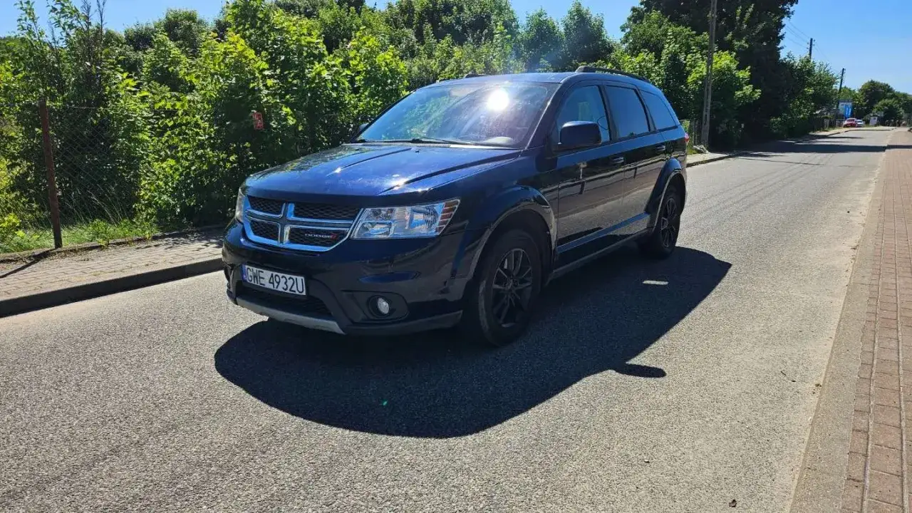 Ciemnoniebieski Dodge Journey stoi na poboczu drogi, otoczony zielenią.