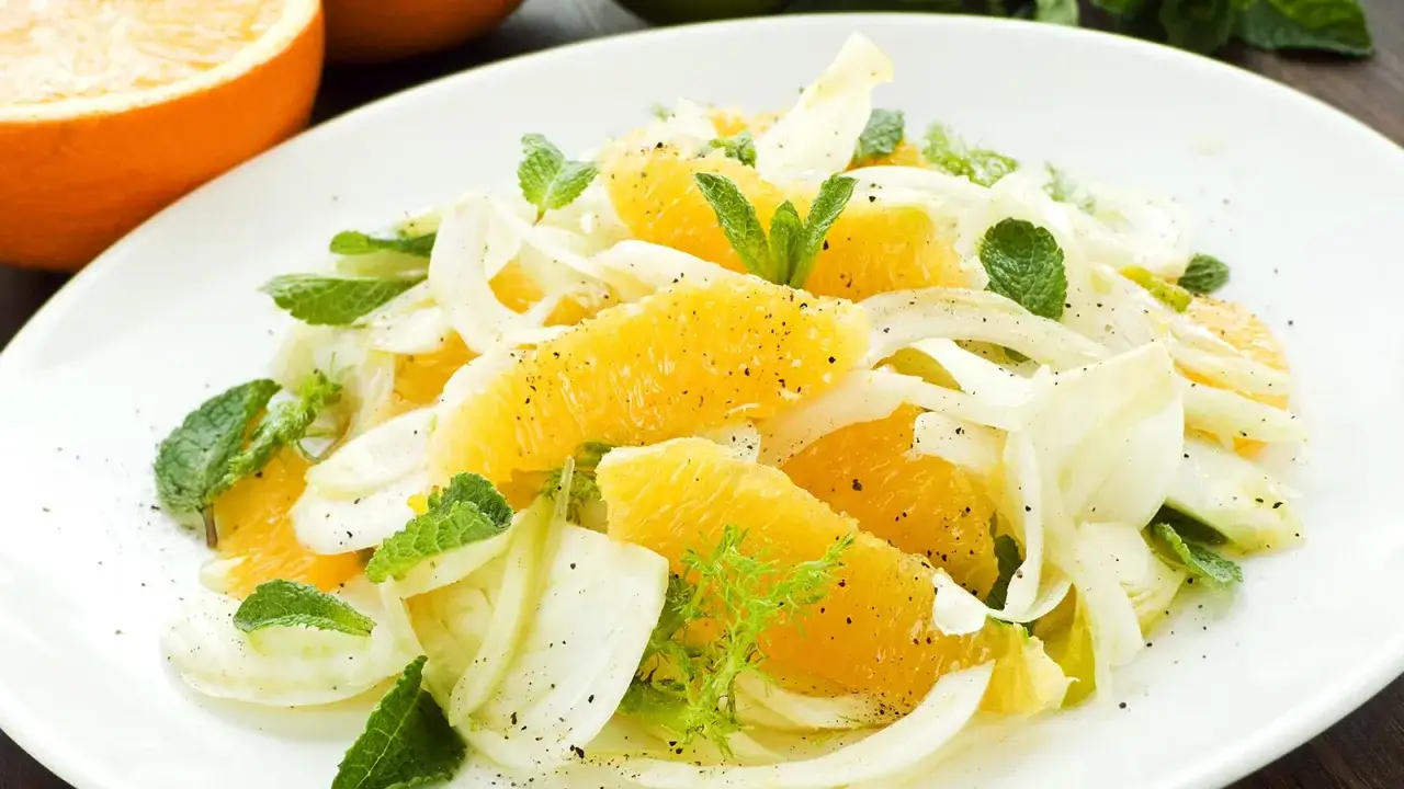 Erfrischender Fenchel-Salat mit saftigen Orangenspalten und Minze, garniert mit schwarzem Pfeffer. Ein leichter Genuss.