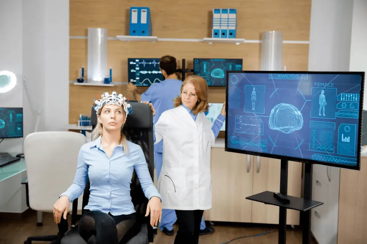 Kobieta w czepku EEG, lekarze analizują dane na ekranach. To może być część diagnostyki, która obejmuje też jakie badania krwi do neurologa.
