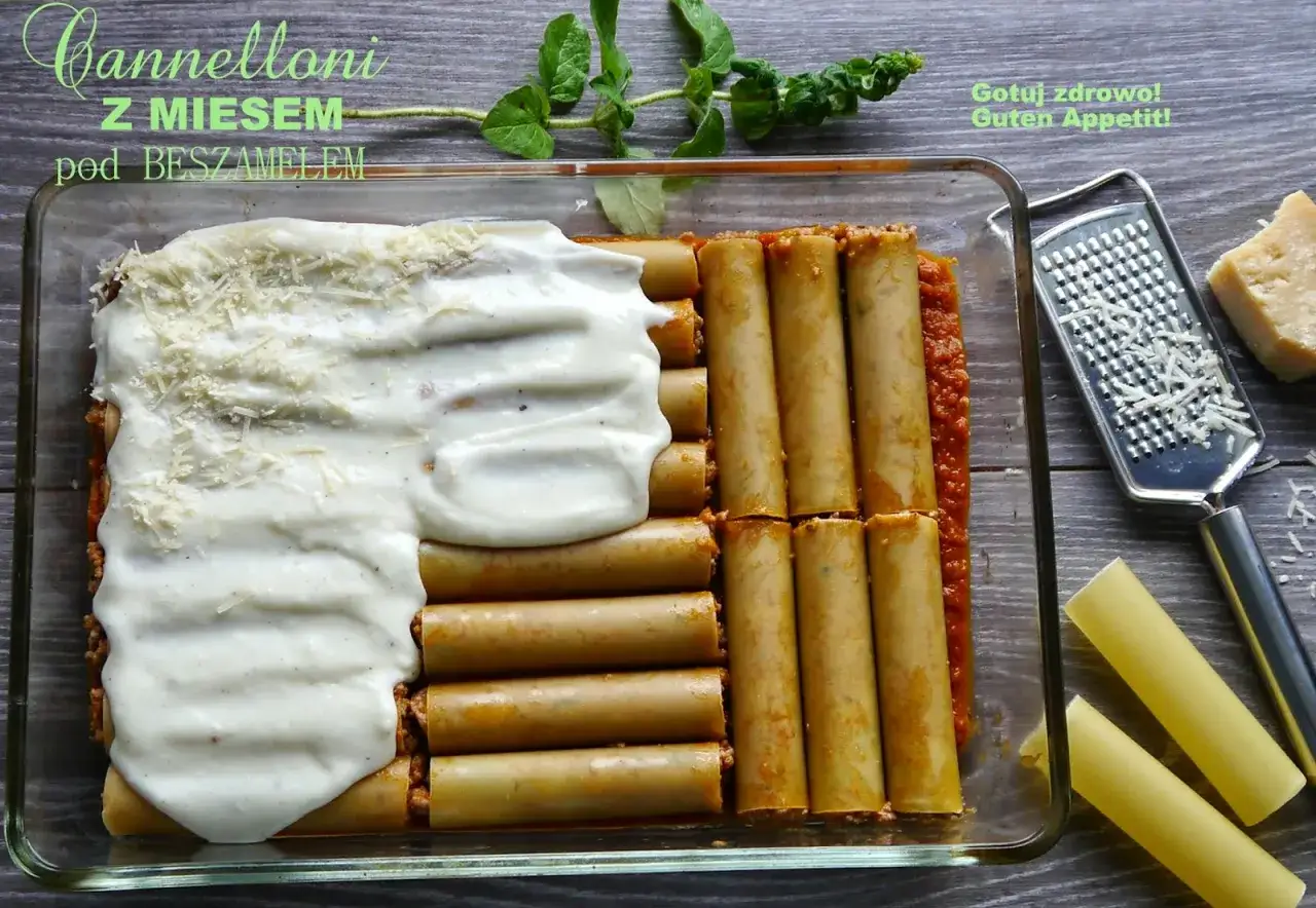 Cannelloni z mięsem mielonym i sosem beszamelowym w naczyniu żaroodpornym, gotowe do pieczenia. Obok tarka i kawałek parmezanu.