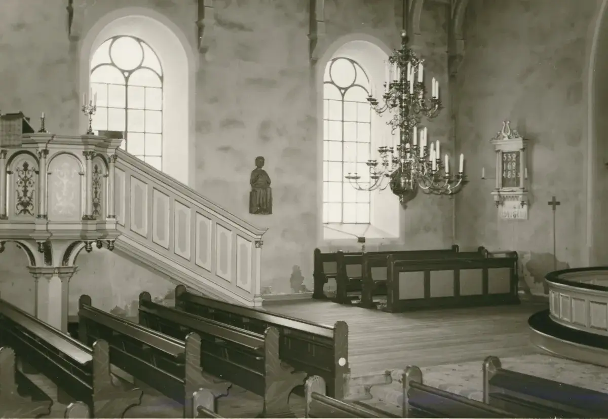 Kyrkans interiör med predikstol, bänkar och en ljuskrona. Altare synonym är inte synligt, men kyrkan är en plats för andakt.