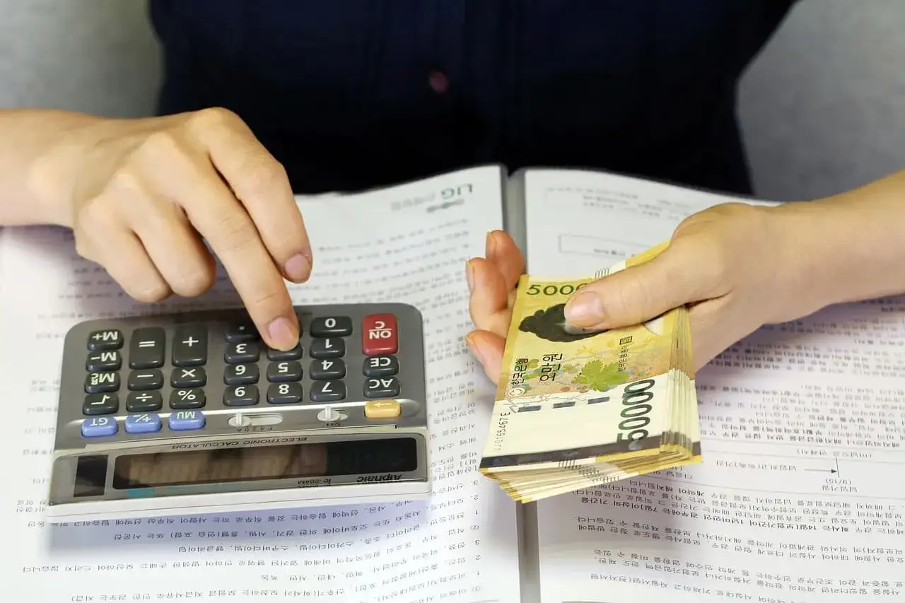 Ręce liczą pieniądze na kalkulatorze. Czy to wynagrodzenie na konto innej osoby, które może zająć komornik?
