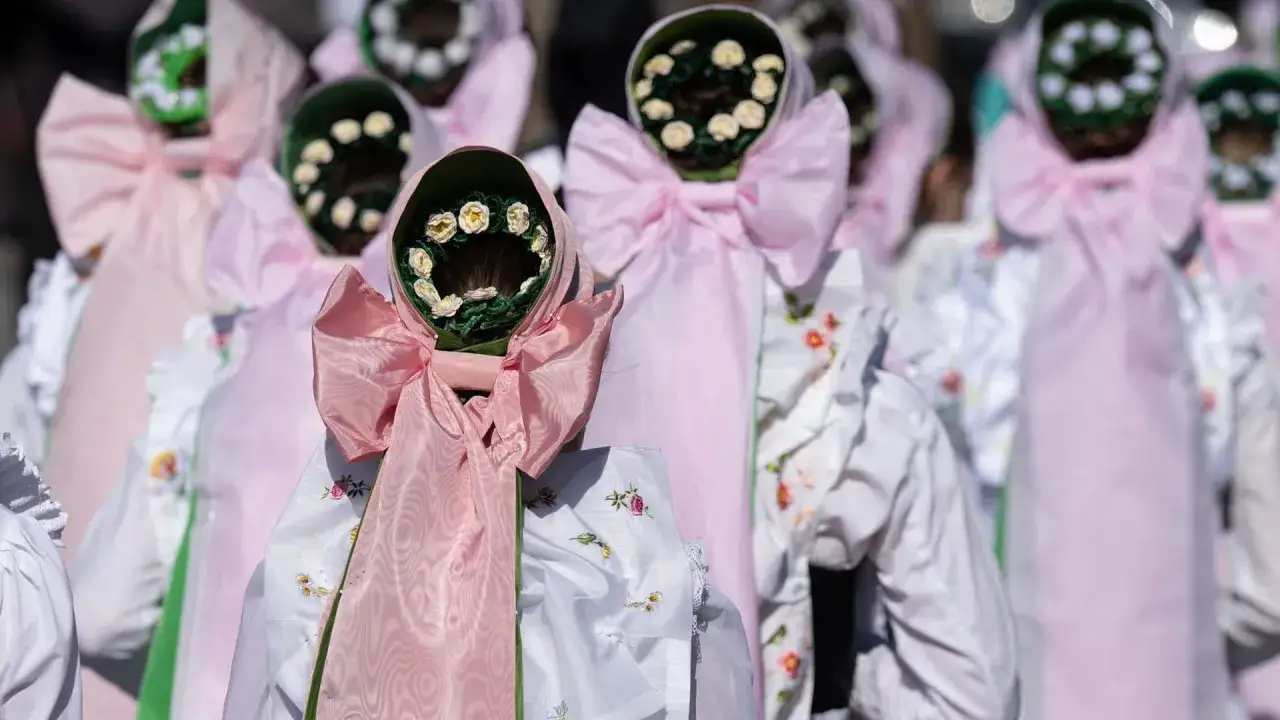 Menschen in traditionellen Trachten mit Blumenkränzen auf dem Kopf, die an Fronleichnamsprozessionen erinnern. Der Ursprung dieser Bräuche ist tief in der Geschichte verwurzelt.