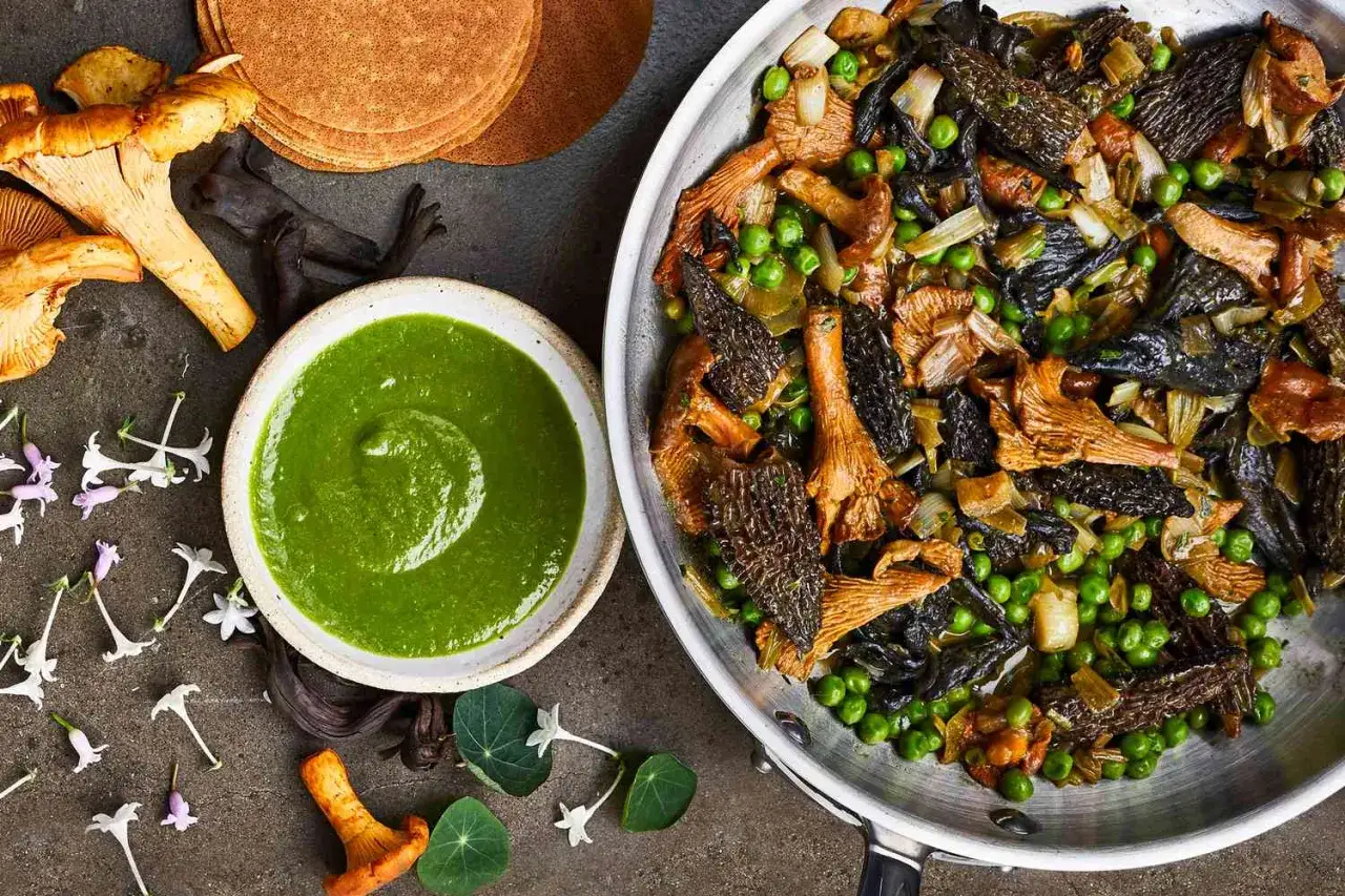 Pfanne voller gebratener Pilze, Erbsen und Lauch, daneben eine Schüssel mit grüner Sauce und frische Kräuter. Ein Festmahl al funghi.