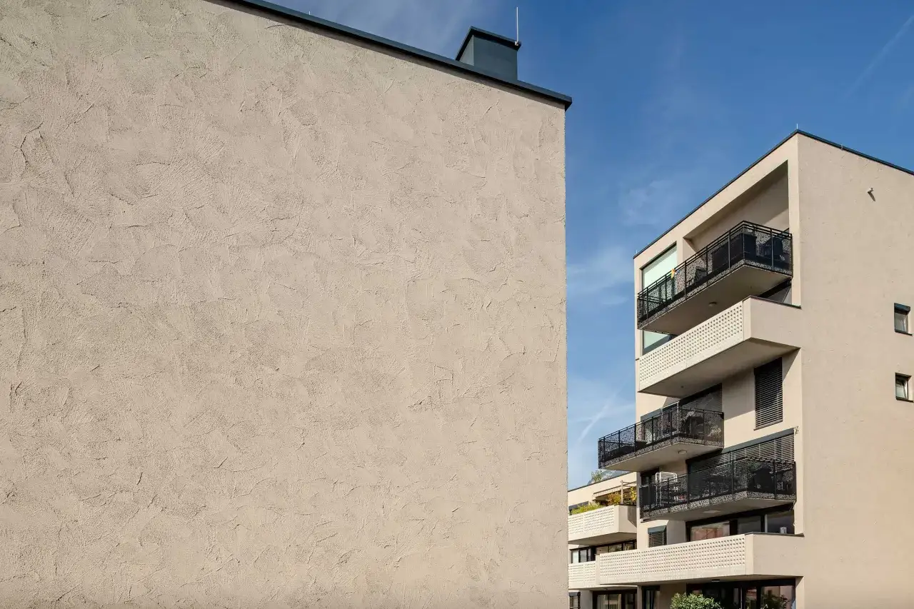 Dettaglio di un muro con finitura intonaco esterno grezzo, che mostra diverse texture e sfumature.