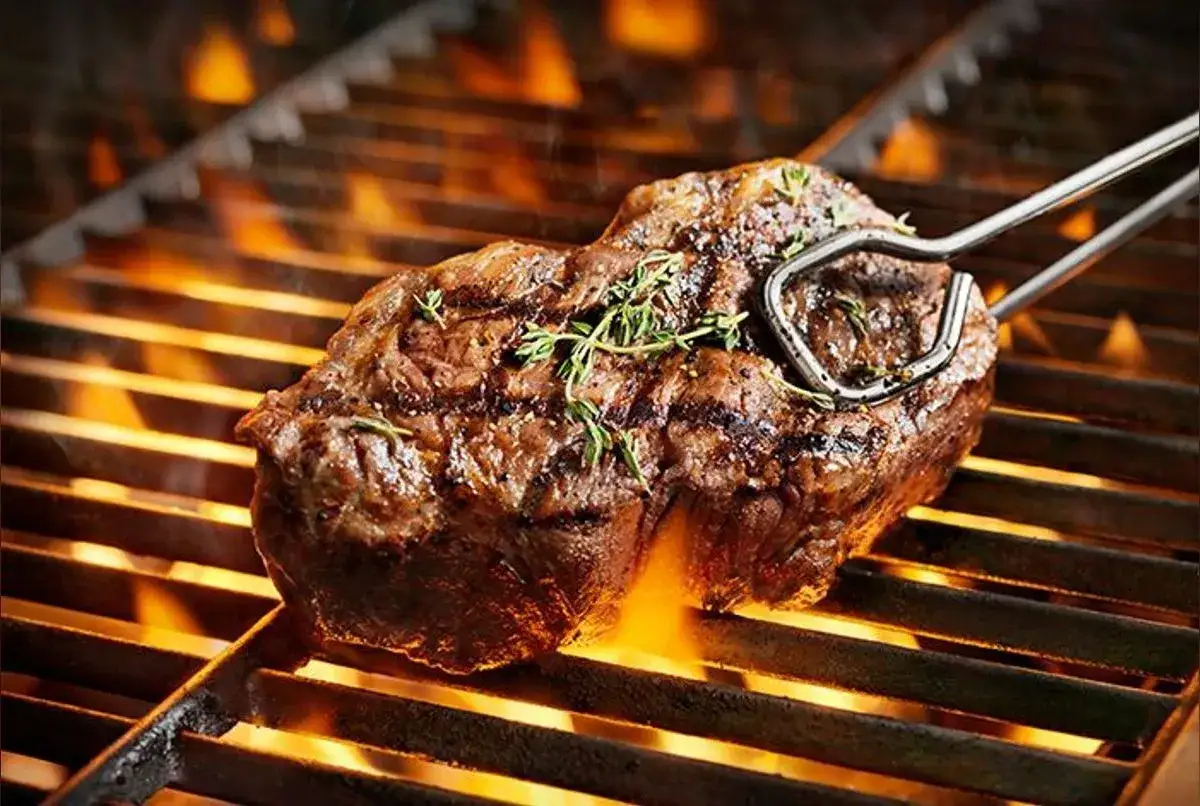 Un savoureux morceau de viande au barbecue, parsemé de thym, grésille sur la grille avec des flammes vives en dessous.