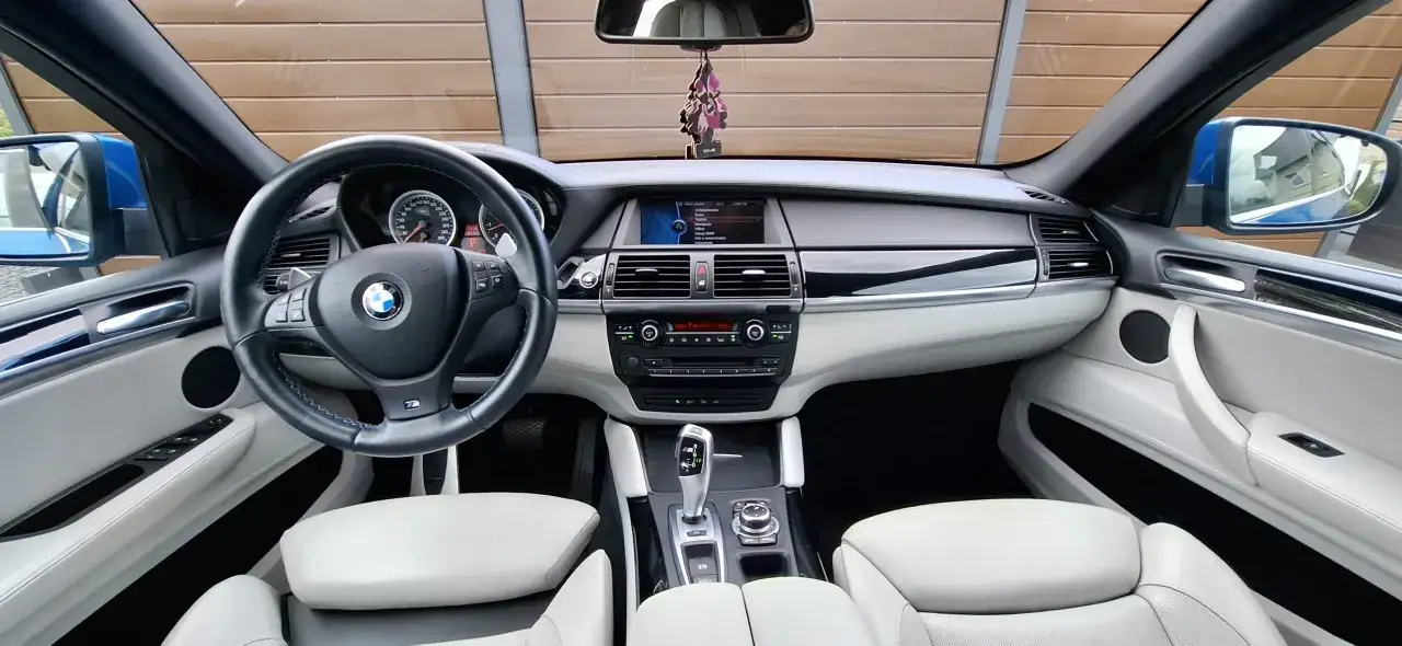 Wnętrze BMW E71 z jasną tapicerką, kierownicą M i ekranem multimedialnym.