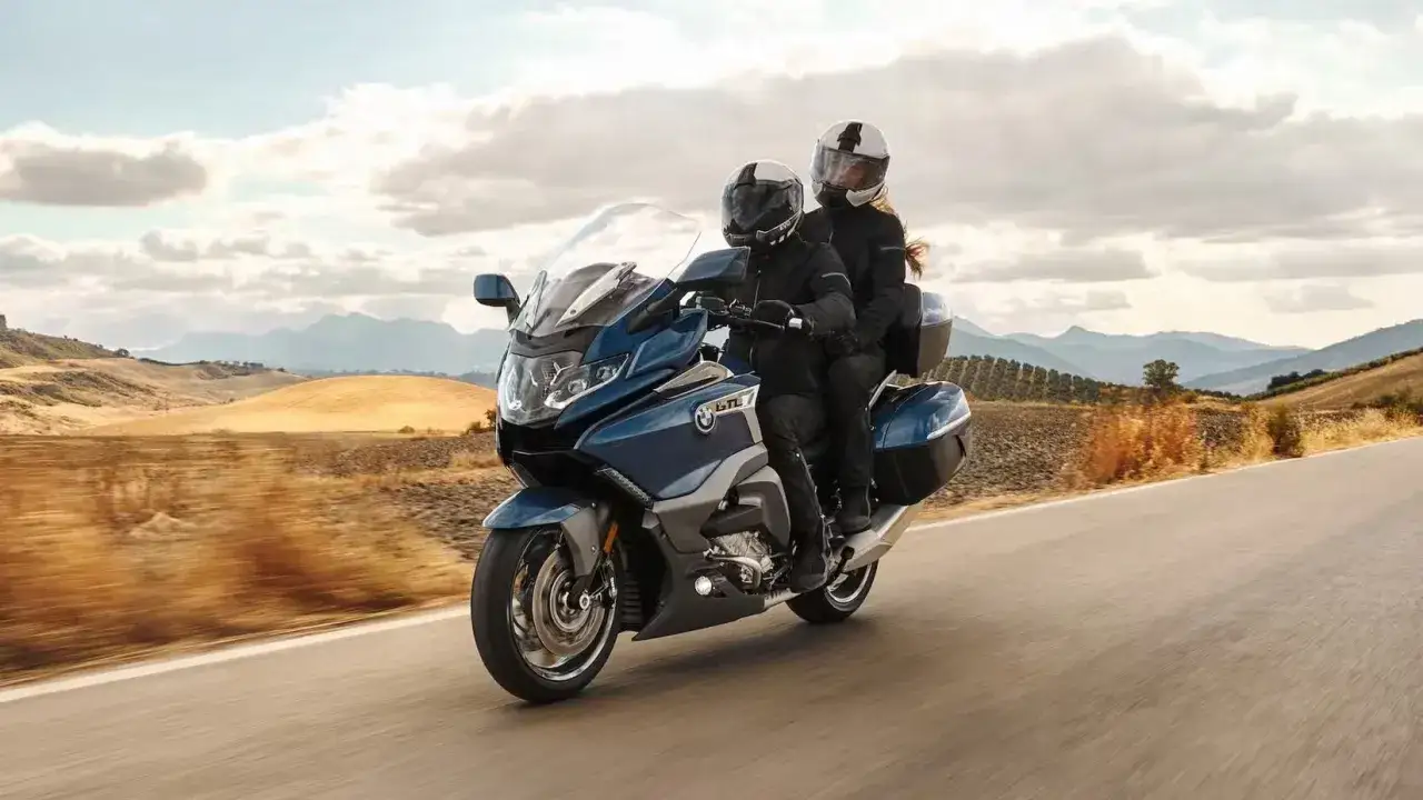Pareja disfrutando de un viaje en una moto azul, ideal para **motos cómodas para viajar**, con un paisaje montañoso de fondo.