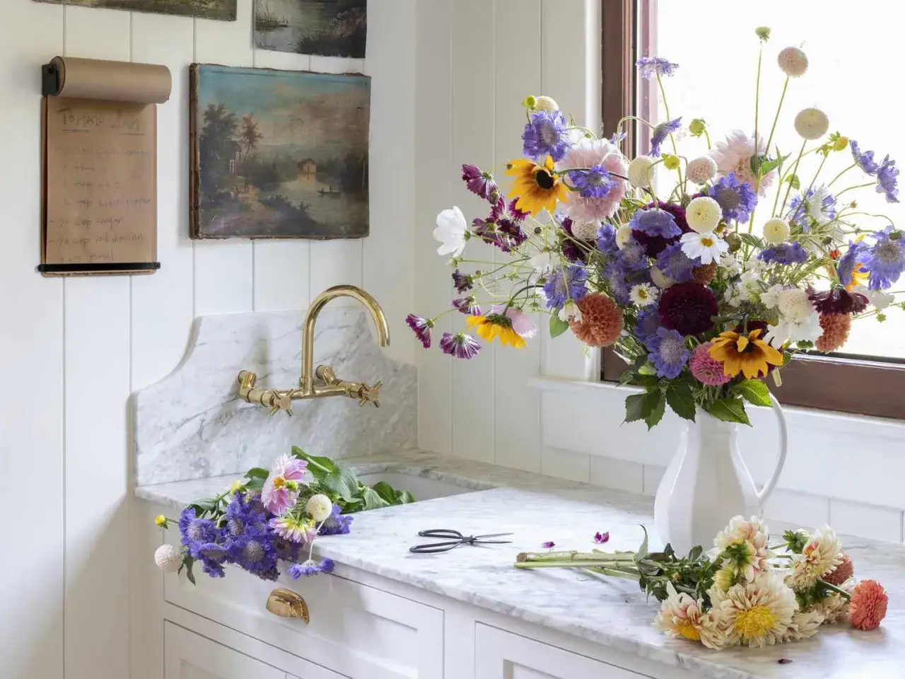 Un grand bouquet de fleurs sauvages dans un pichet blanc, pr&ecirc;t &agrave; &ecirc;tre arrang&eacute;. Des fleurs coup&eacute;es et des ciseaux sur le comptoir en marbre, pour savoir comment conserver un bouquet de fleurs.