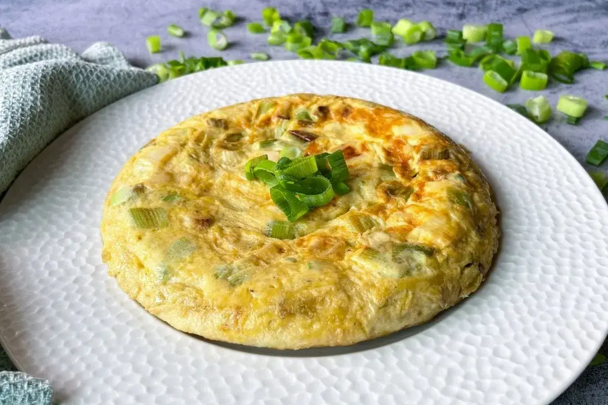 Tortilla dorada con trozos de ajos tiernos, decorada con más ajos picados.